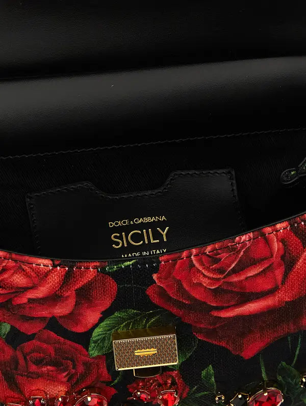 Close-up of a Dolce &amp; Gabbana Sicily handbag featuring a black leather interior flap with gold branding, a red rose print fabric, and a gold-tone clasp.
