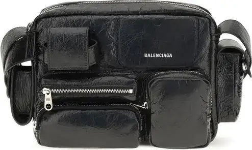 A black Balenciaga shoulder bag made of textured leather, featuring multiple zippered pockets and a silver-tone logo on the front, set against a plain white background.
