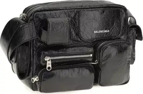 A black Balenciaga textured faux-leather crossbody bag with multiple zippered pockets and a silver-tone logo on the front, shown against a plain white background.