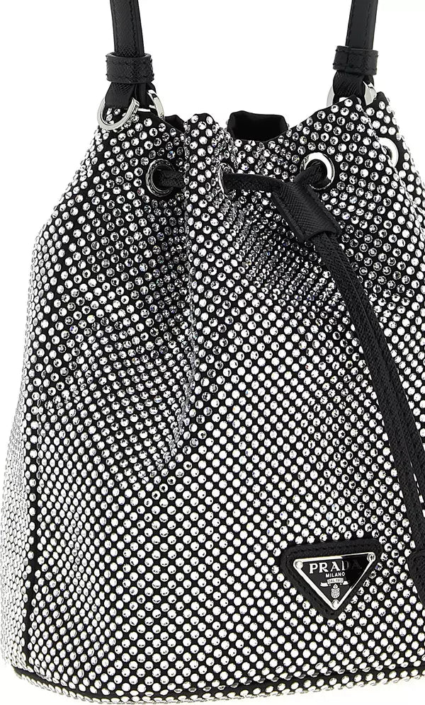 A Prada bucket bag covered in silver rhinestones with black leather trim, drawstring closure, and a silver-tone triangular Prada logo plaque on the front.