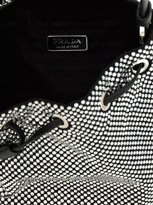 Close-up of a Prada handbag interior and exterior detail, showing a black Prada Made in Italy metal plaque, black leather trim, silver-tone hardware, and a black-and-white rhinestone mesh pattern.