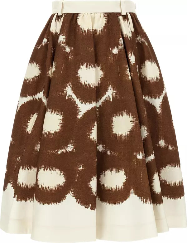 A pleated A-line skirt featuring a brown and cream ikat-style circular pattern, with a solid cream border at the hem and a matching cream waistband.