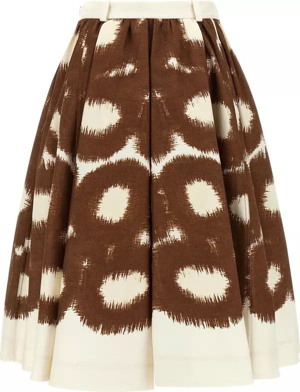 A pleated A-line skirt featuring a brown and cream ikat-style circular pattern, with a solid cream waistband and hem.