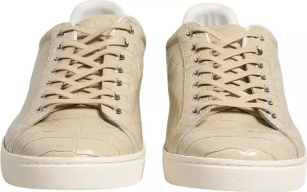 A pair of beige crocodile-embossed leather low-top sneakers with matching laces and white soles, shown from a front-facing perspective on a white background.