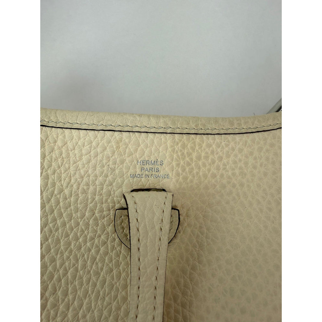 Close-up of a beige leather bag with 'Hermes' branding on a light gray background