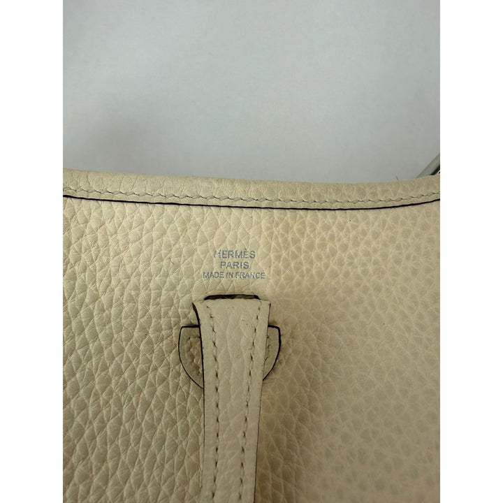 Close-up of a beige leather bag with 'Hermes' branding on a light gray background
