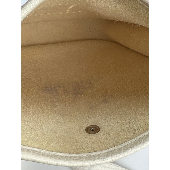 Close-up of a beige leather surface with a button, possibly from a bag or wallet.