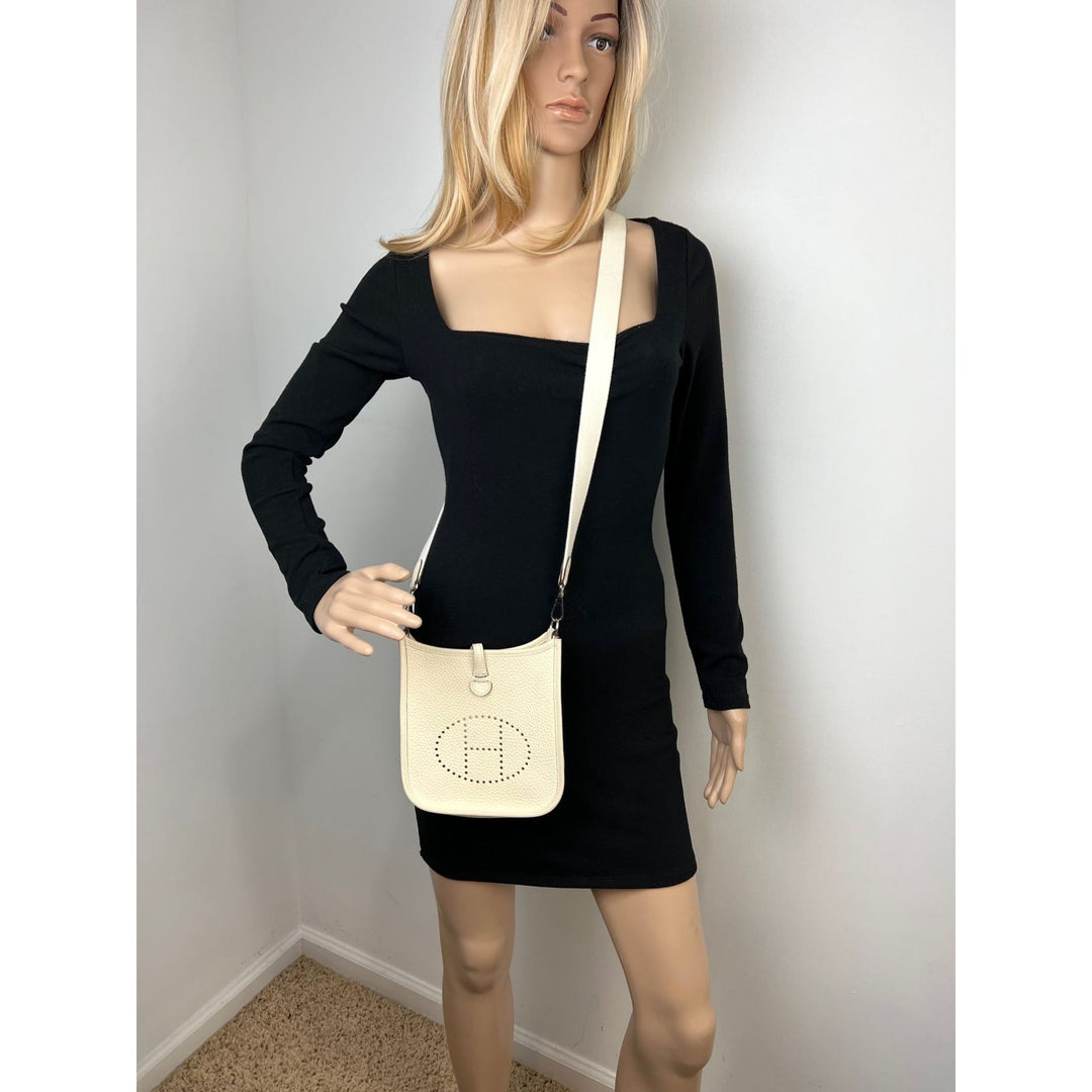 Mannequin wearing a black dress with a beige handbag against a plain background