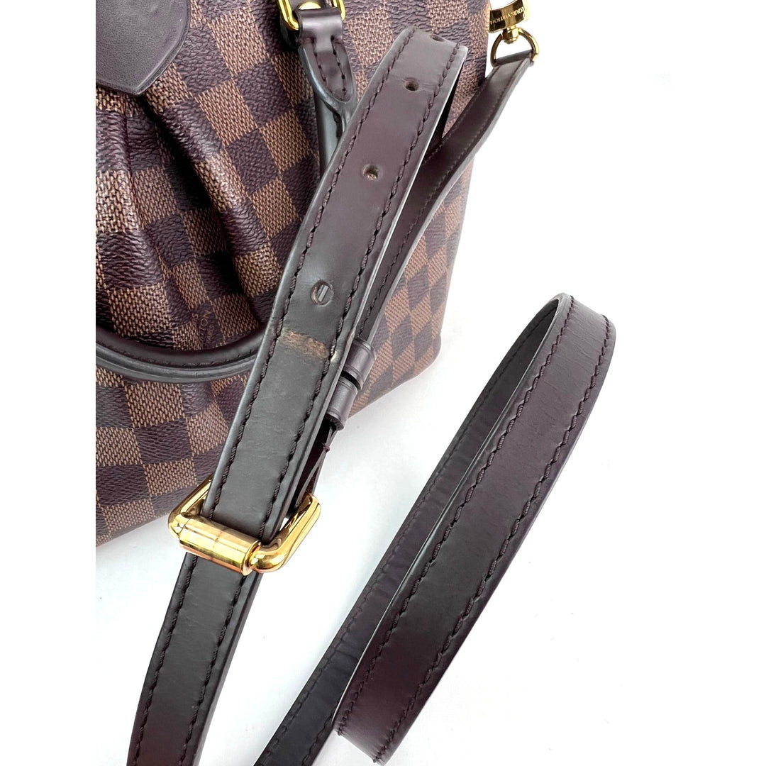Close-up of a brown patterned handbag with a gray strap and gold hardware on a white background.