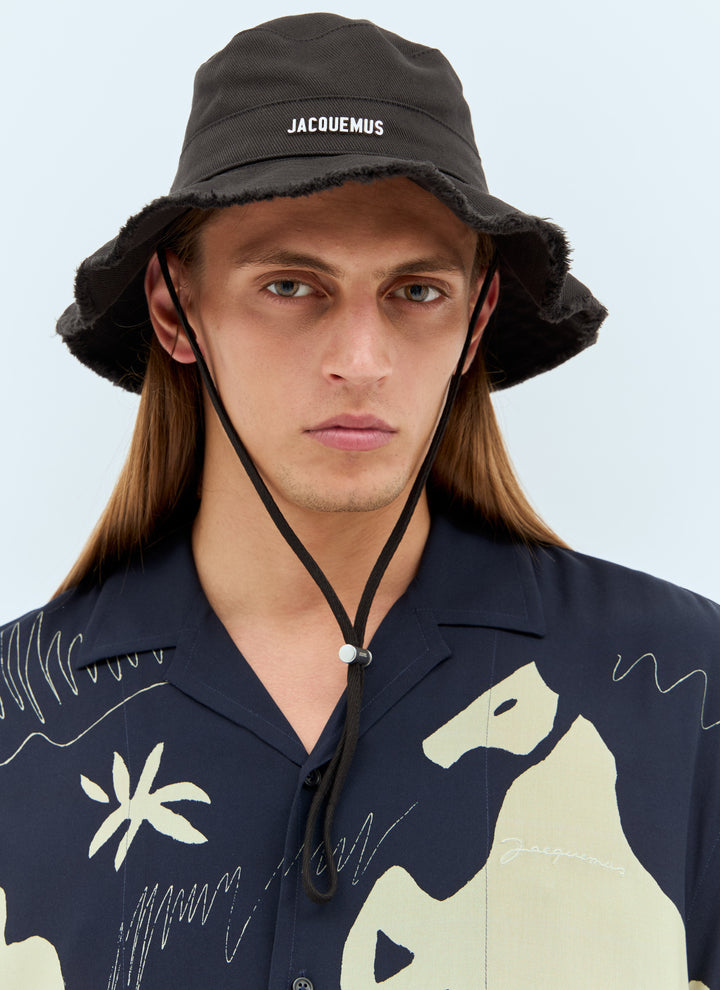 Man wearing a black bucket hat with 'Jacquemus' branding and a dark shirt with light designs.