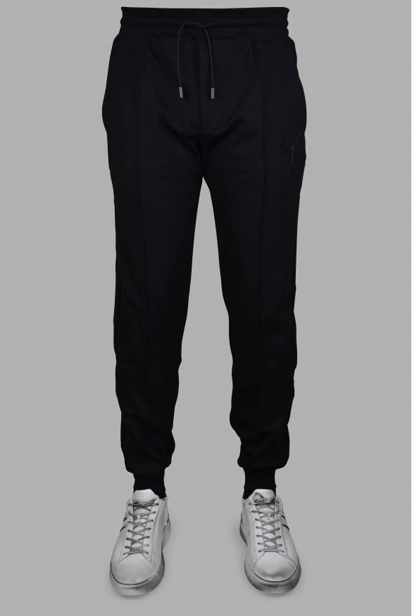 Black jogger pants worn with white sneakers on a gray background