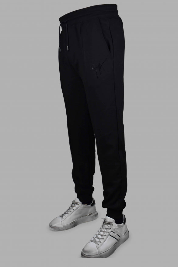 Black jogger pants worn with white sneakers on a gray background
