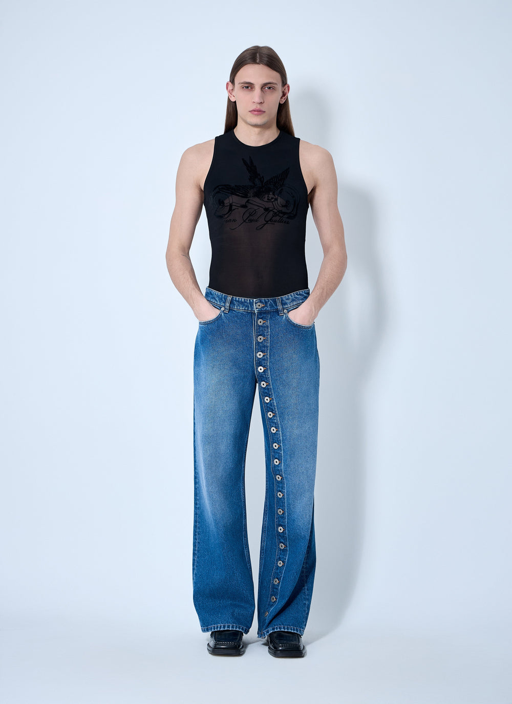 Person wearing a black sleeveless top and blue jeans with button details on a white background