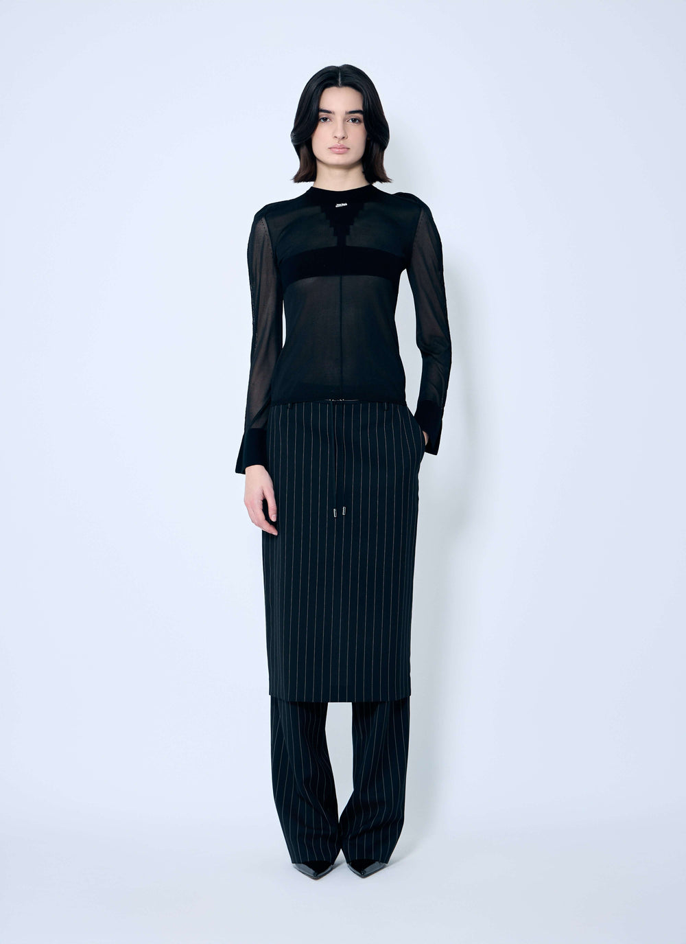 Person wearing a black outfit with sheer sleeves on a white background