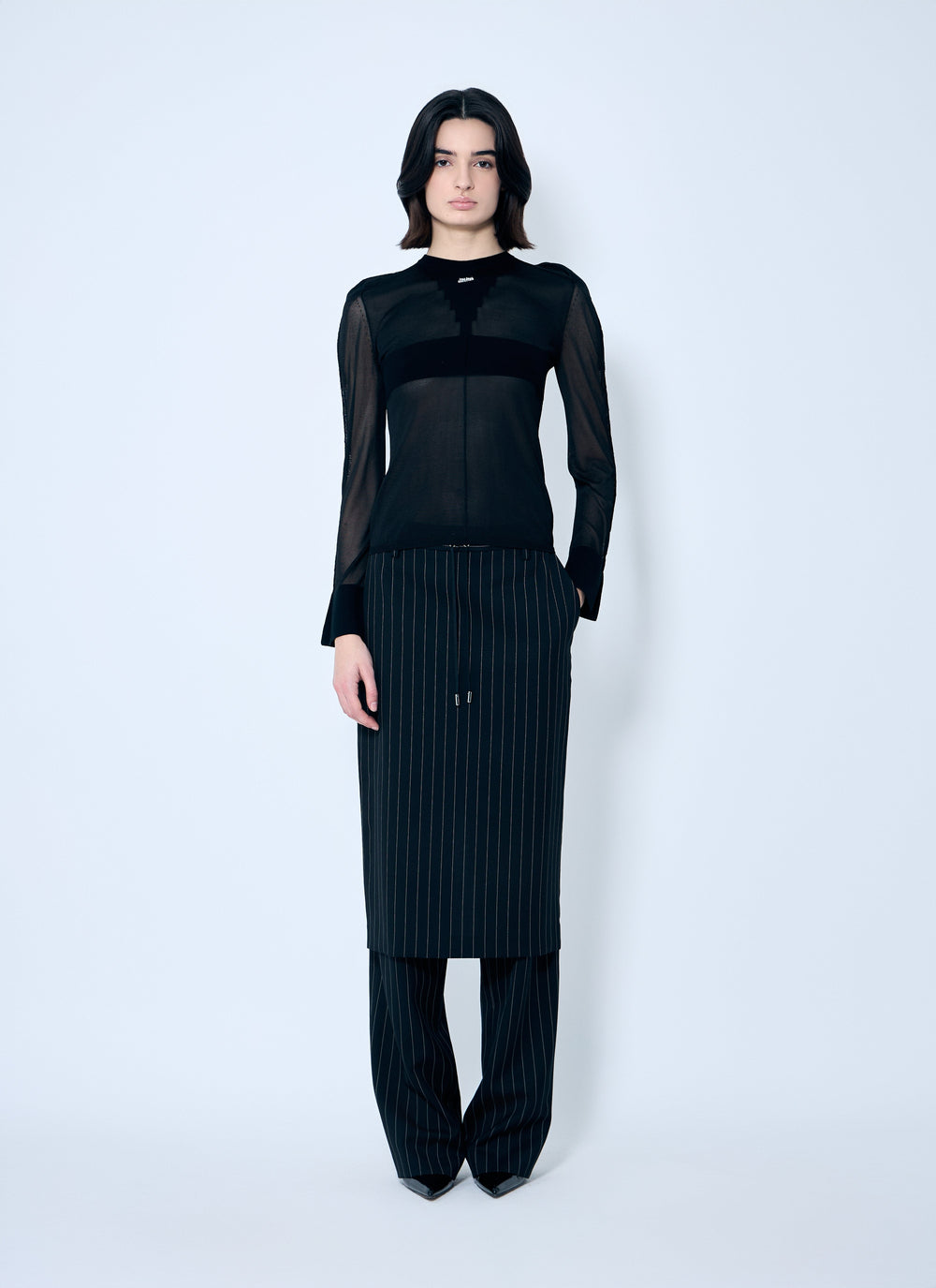 Person wearing a black outfit with sheer sleeves on a white background