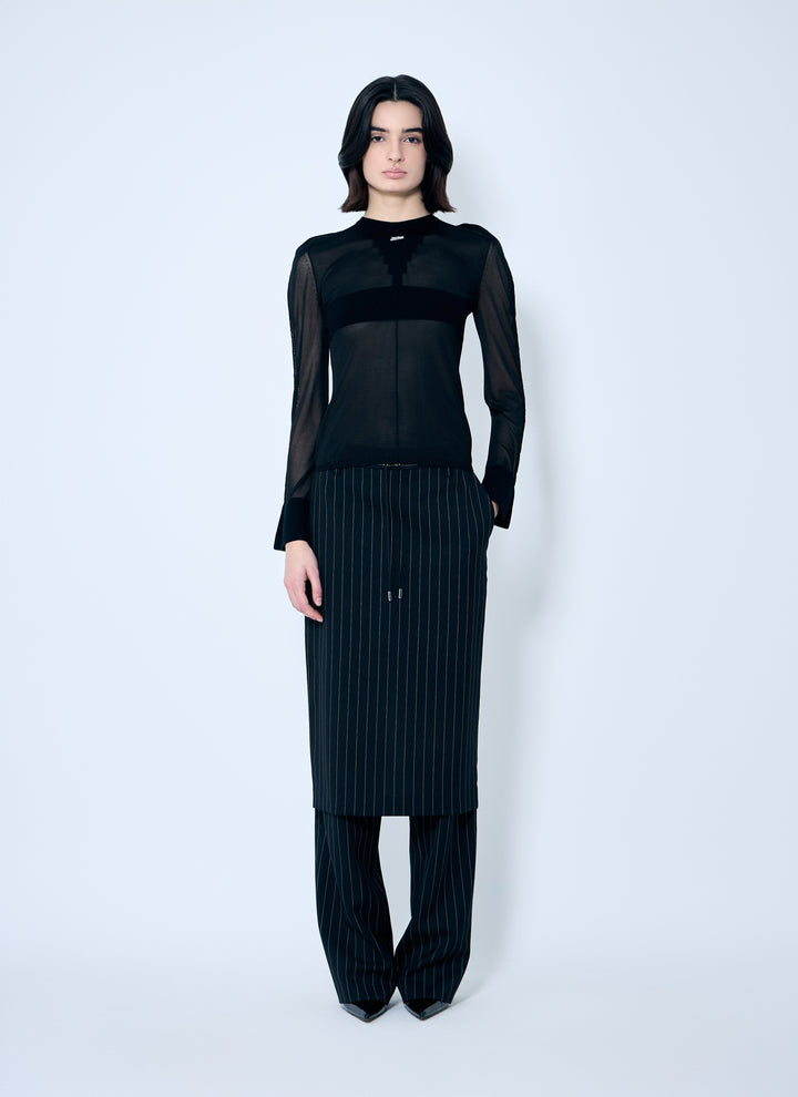 Person wearing a black outfit with sheer sleeves on a white background