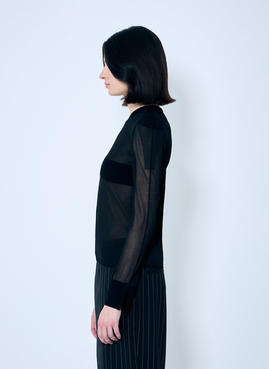 Person wearing a black sheer top and dark pants against a white background