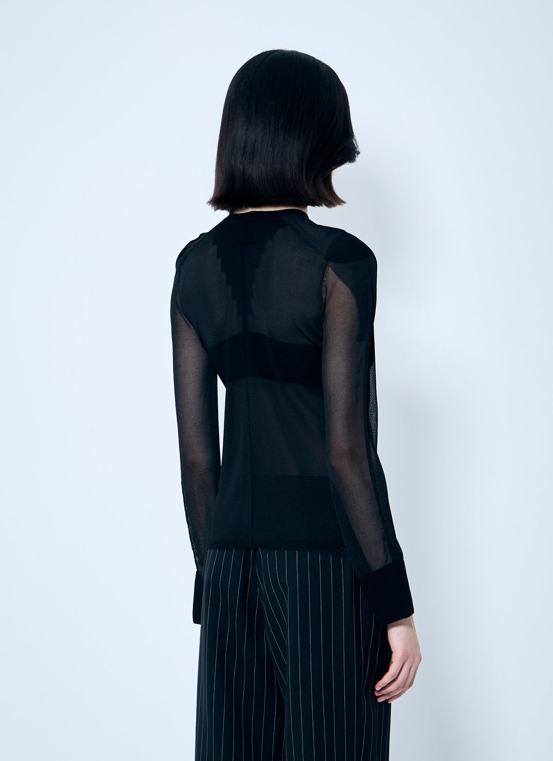 Person wearing a black sheer top and dark pants against a white background