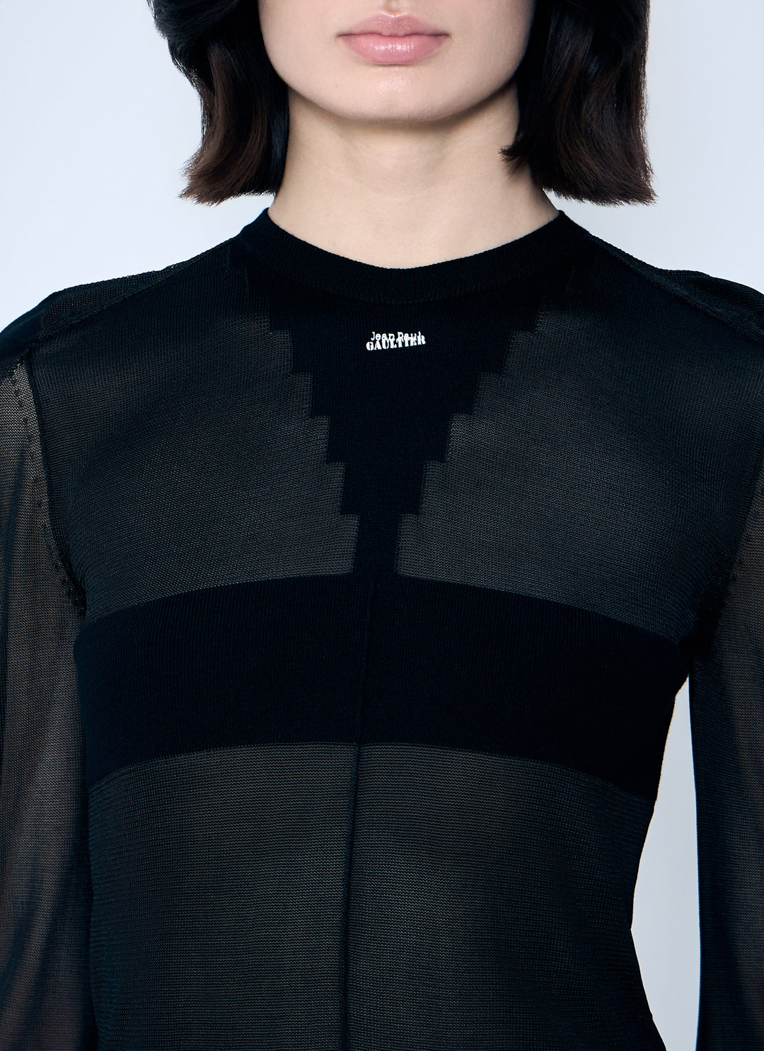 Person wearing a black outfit with a brand logo on a light gray background