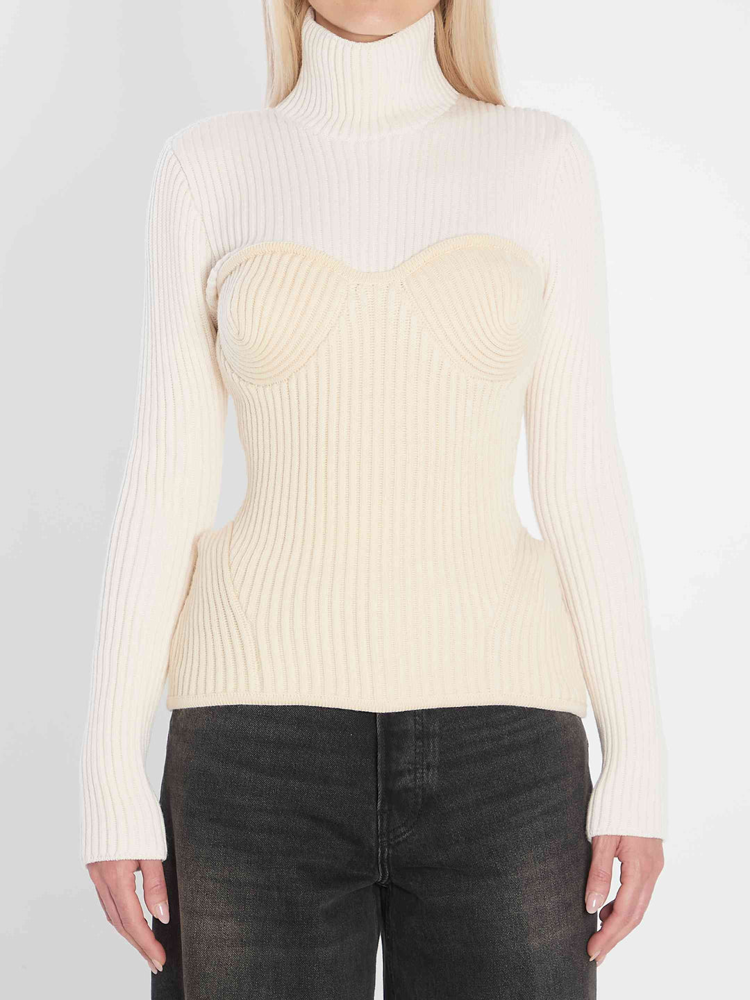 Person wearing a cream ribbed sweater over a strapless top with dark jeans on a light gray background