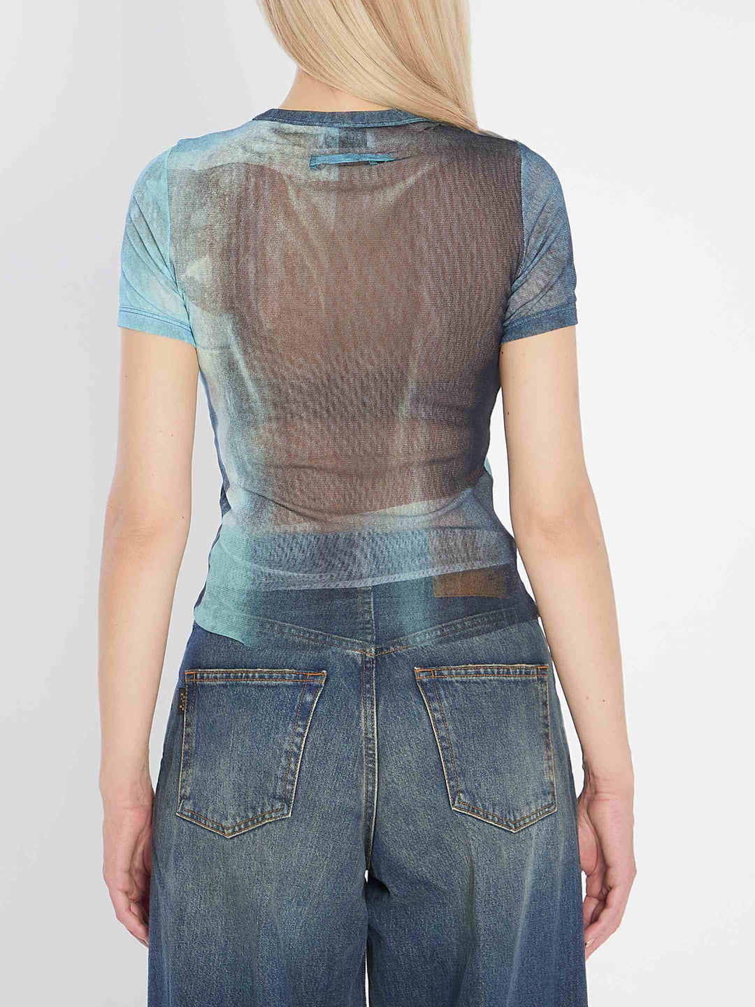 Person wearing a sheer top and jeans with a plain background