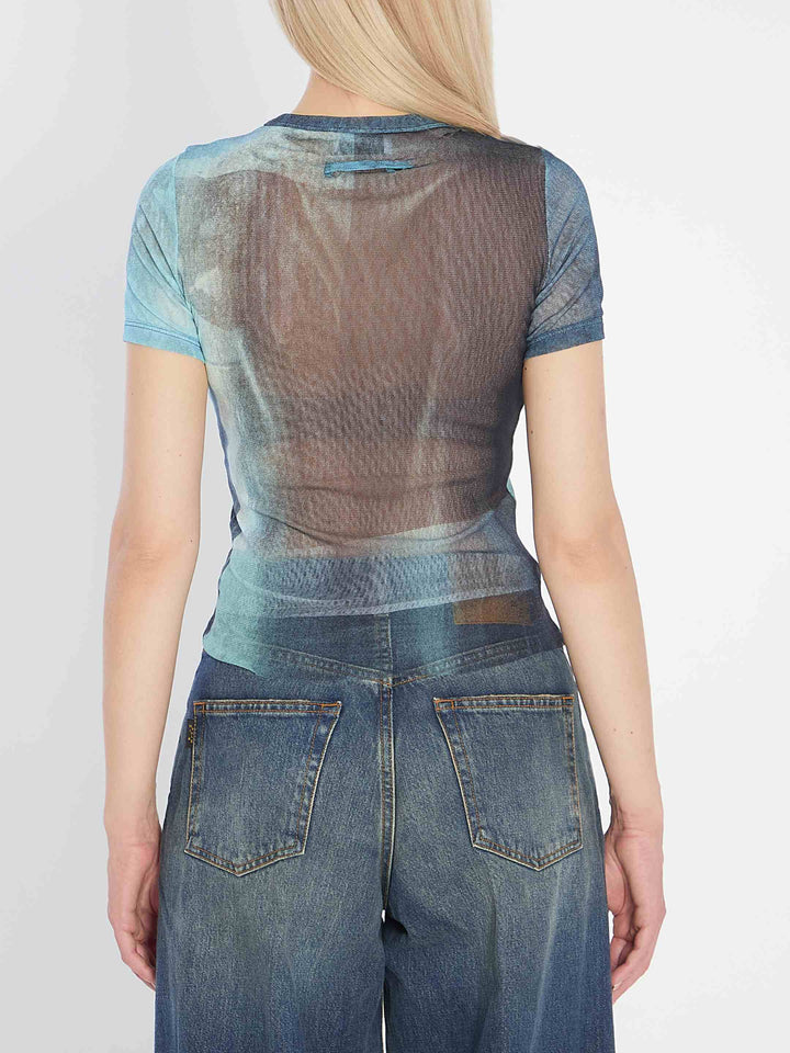 Person wearing a sheer top and jeans with a plain background