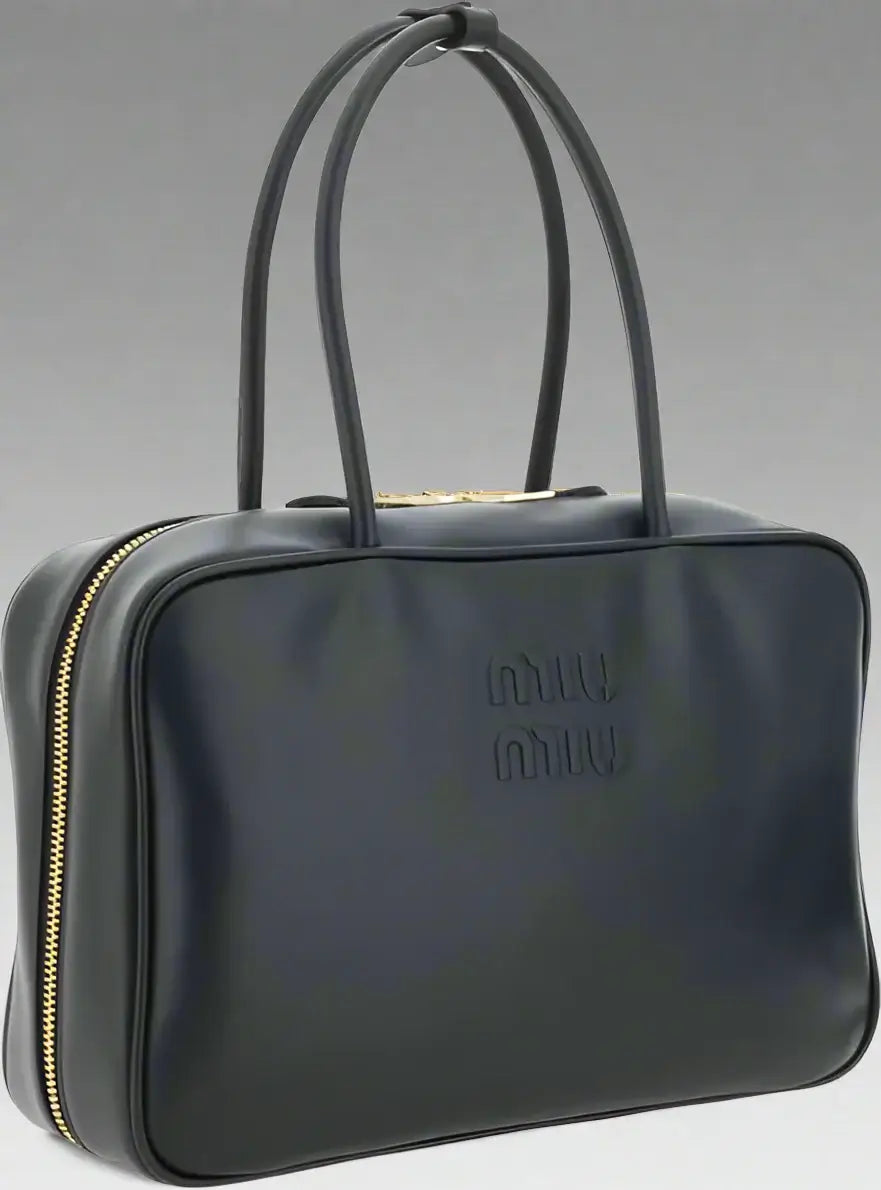 Black handbag with gold zipper and 'miu miu' logo on a white background