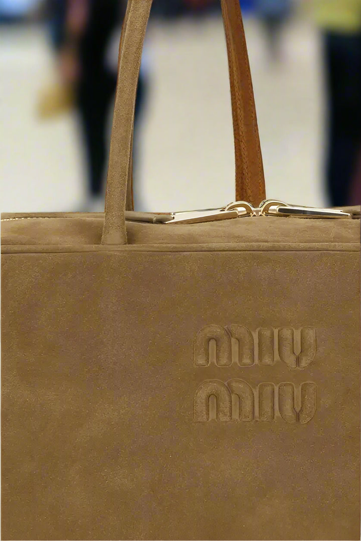 Brown suede handbag with 'milly' branding on a white background