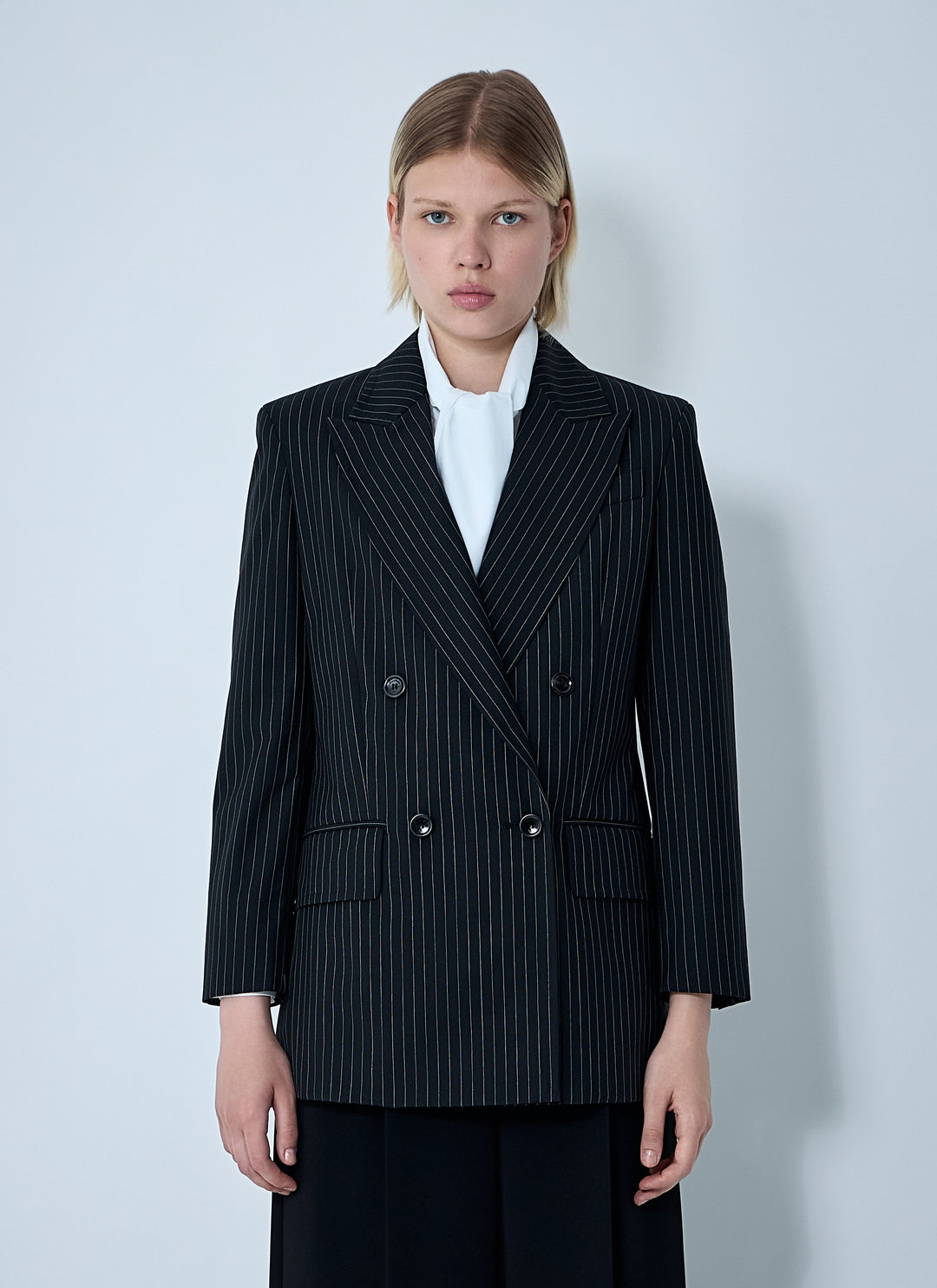 Woman wearing a black pinstripe blazer over a white shirt on a light gray background