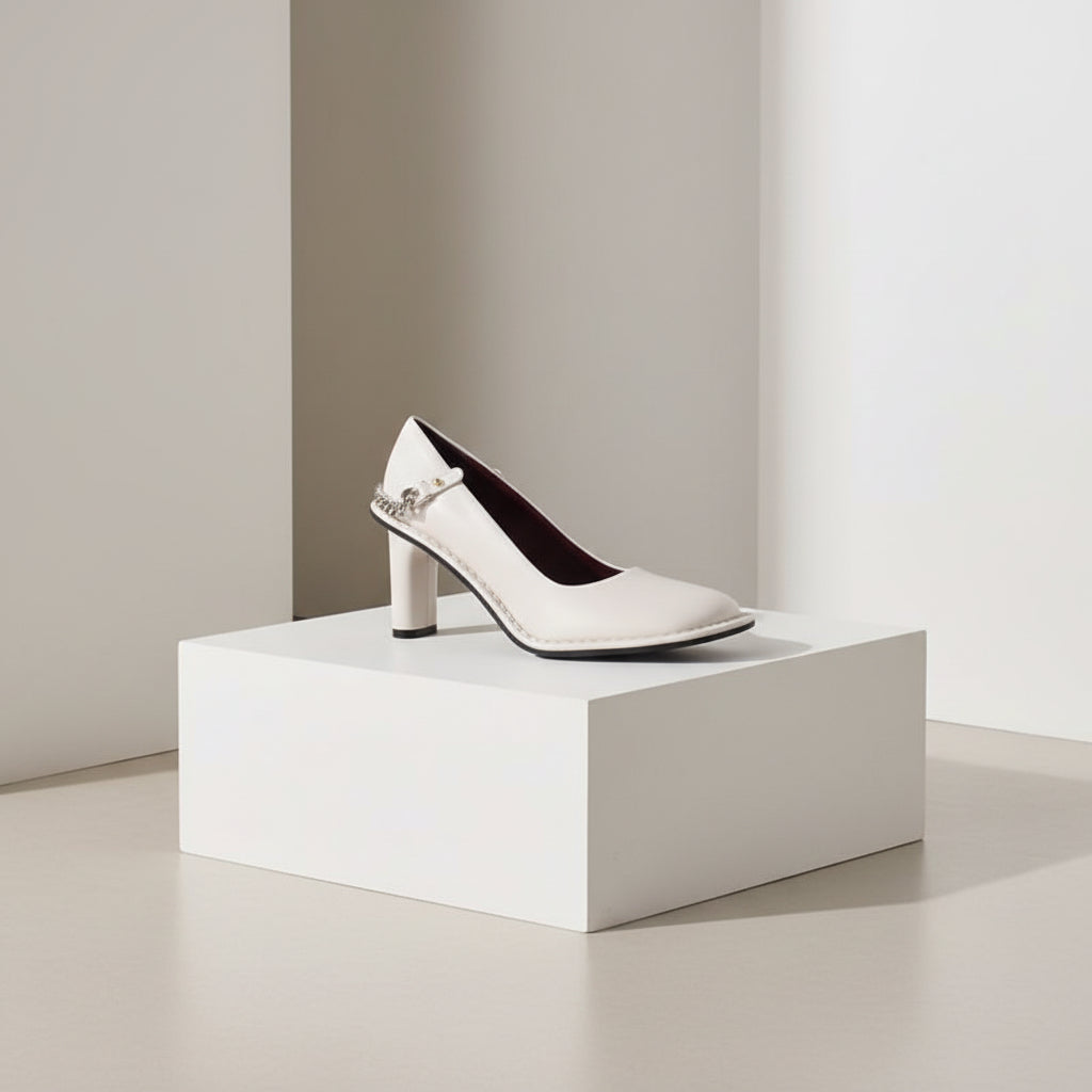 White high-heeled shoe with a small chain detail on a white background