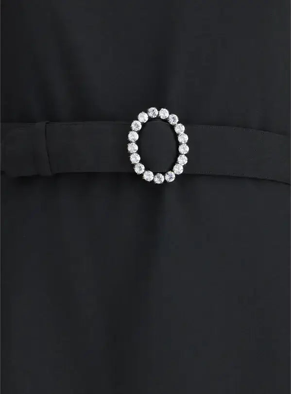 Black dress with a decorative belt featuring a circular crystal buckle on a plain background