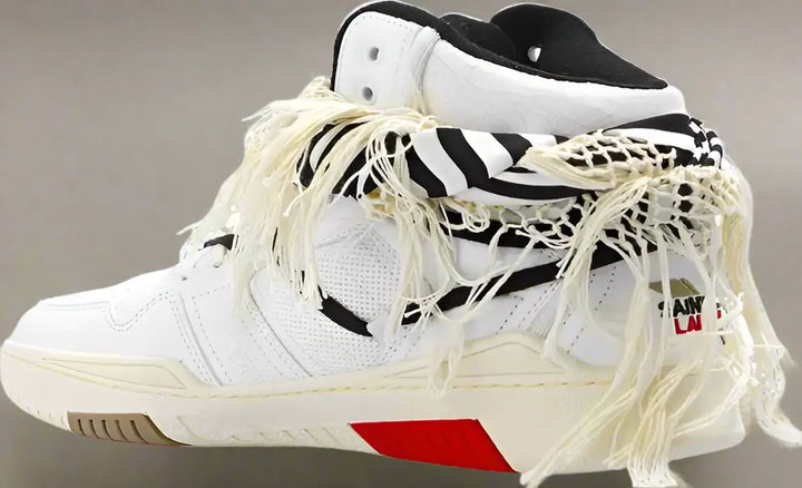 White sneakers with black and red accents and frayed laces on a white background