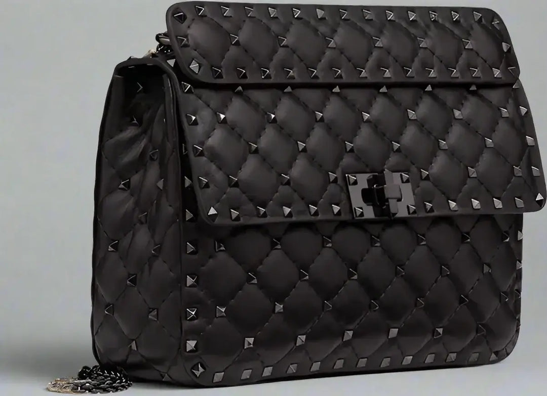 Black quilted handbag with studs on a light gray background