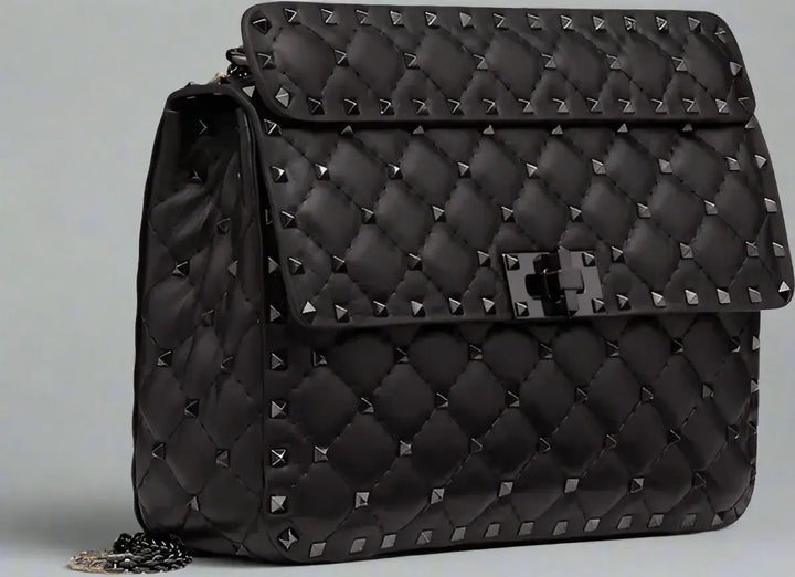 Black quilted handbag with studs on a light gray background