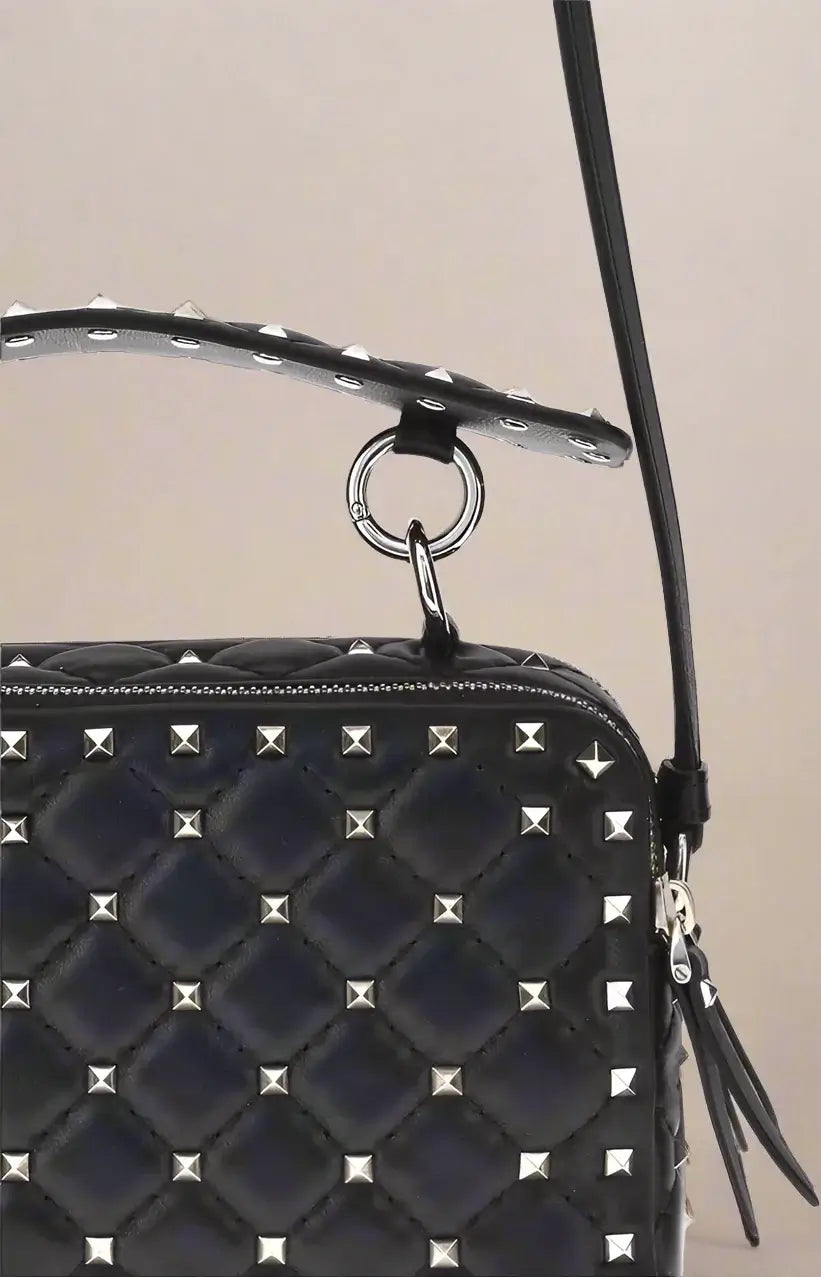 Black quilted handbag with silver studs and a black strap on a white background