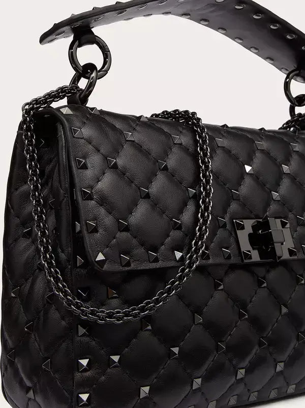 Black quilted handbag with studded details and a chain strap on a light gray background