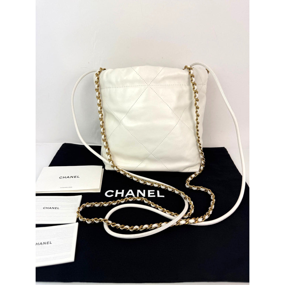 White quilted handbag with gold chain on a black surface, with Chanel branding visible.