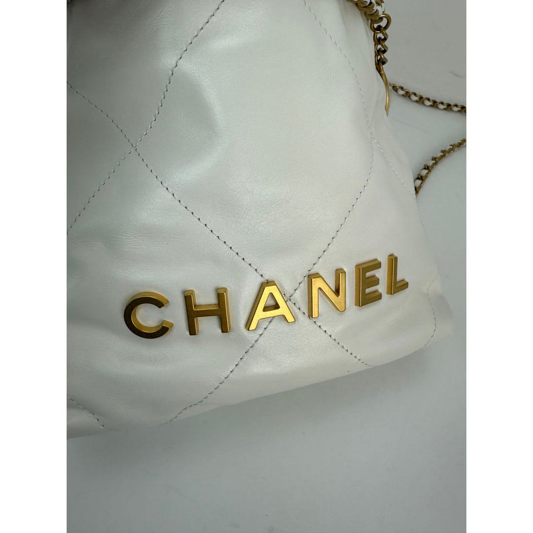 White quilted handbag with gold 'Chanel' logo on a light gray background