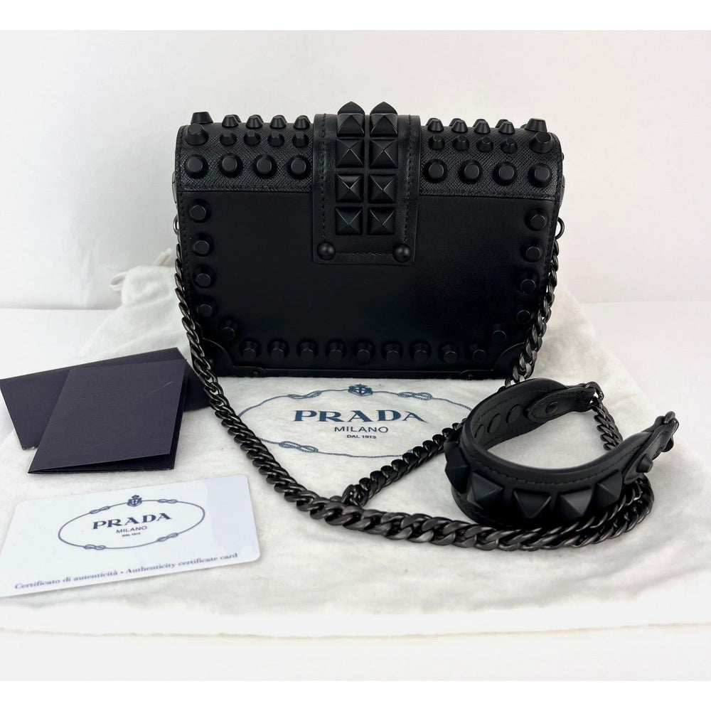 Black studded Prada handbag on a white background with authenticity card.